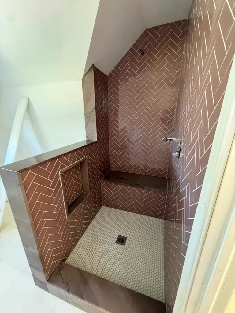Herringbone tile shower with niche, bench and stone half wall