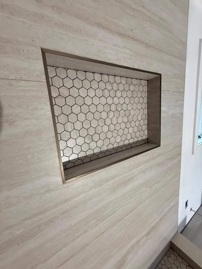 Hexagon mosaic niche set into a travertine shower wall