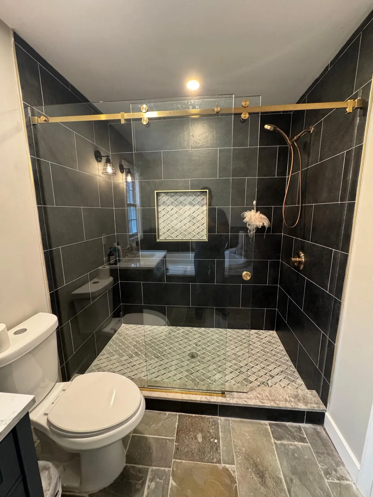 Sliding glass door with gold rail on a dark tile shower
