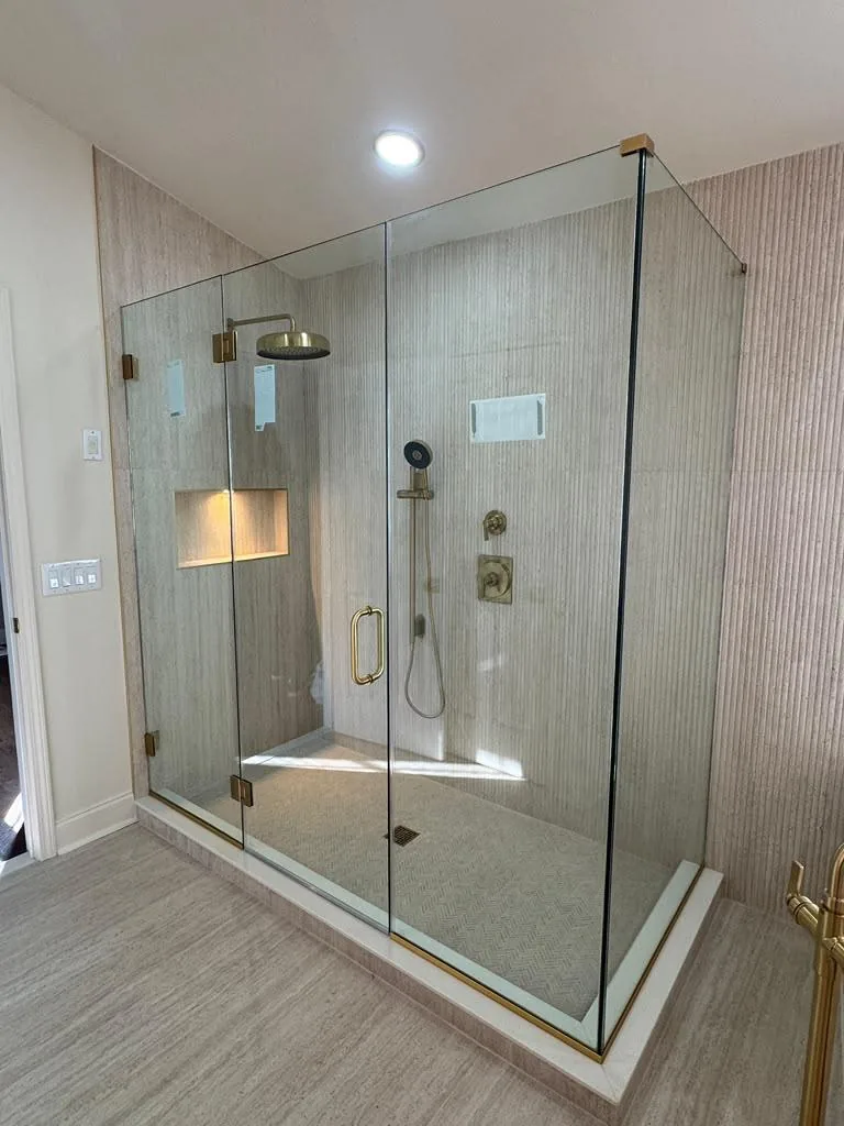 Corner frameless glass shower enclosure with gold hardware and built-in bench